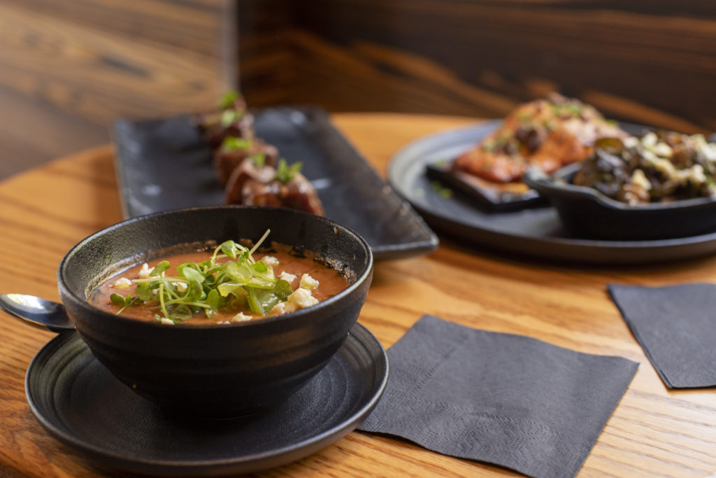 Bowl of soup with herbs alongside a plated barbecue meal